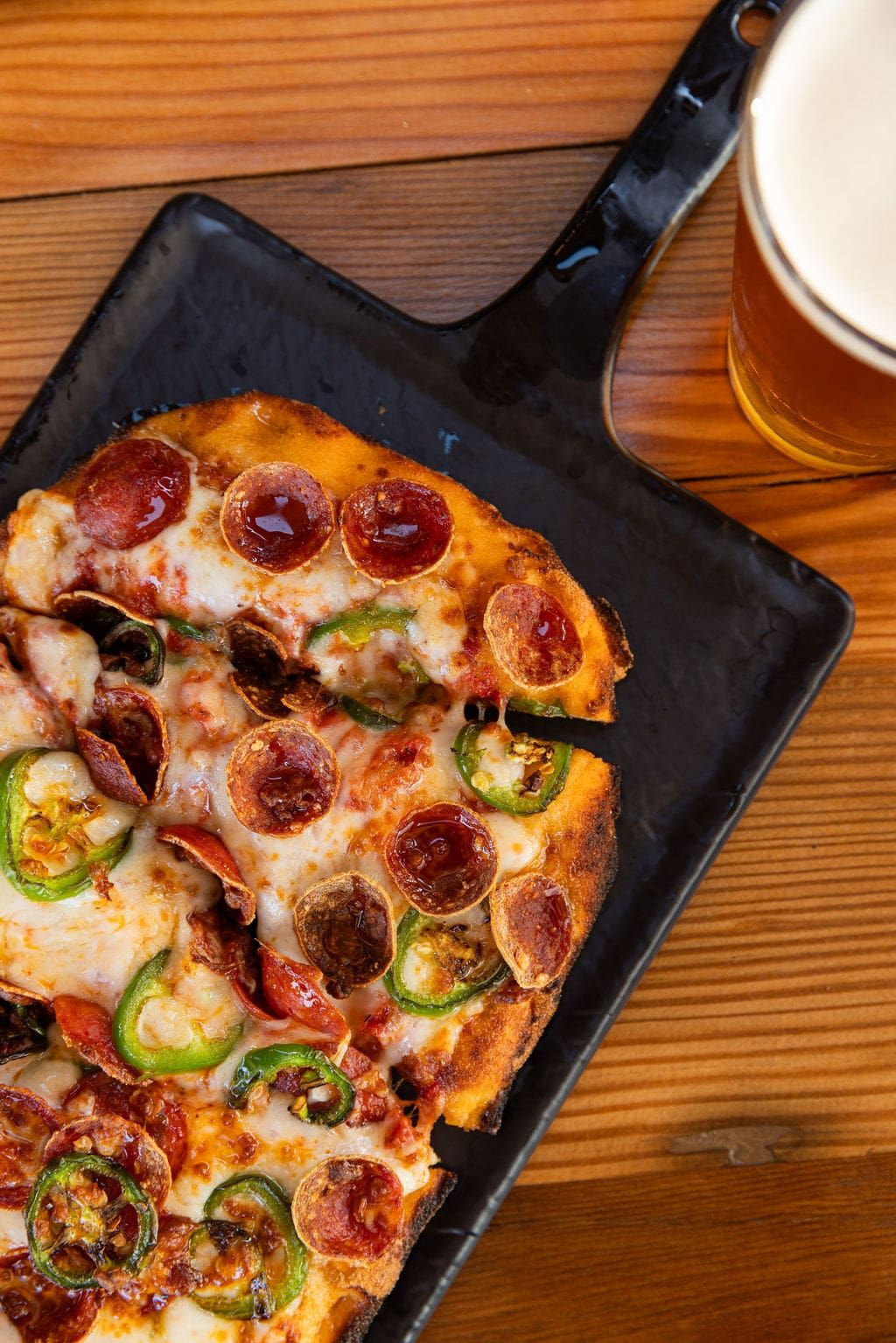 A pepperoni and jalapeño pie served on cast iron with a beer alongside
